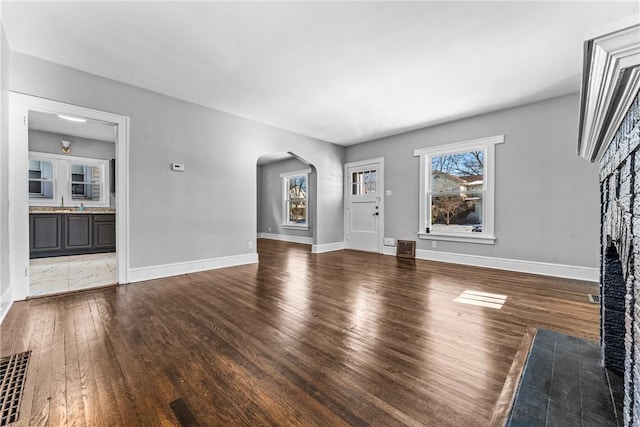 380 Spencer Ave, Sharon, PA 16146 - unfurnished living room featuring wood finished floors, visible vents, arched walkways, baseboards, and a brick fireplace