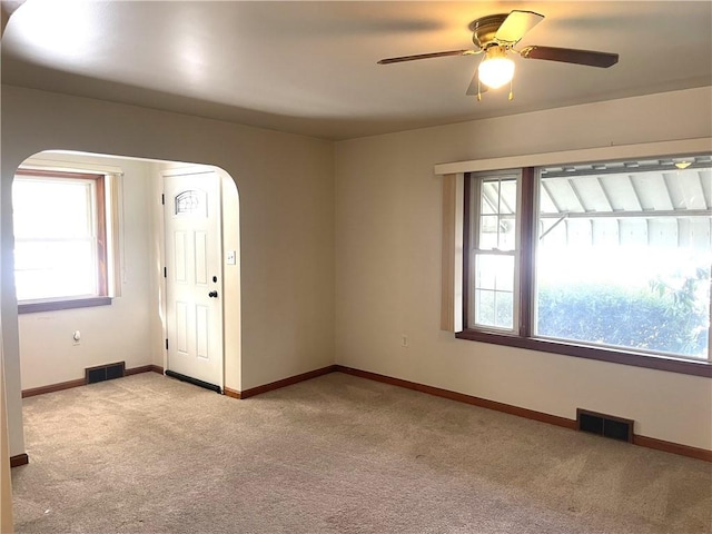 empty room with plenty of natural light, light colored carpet, and ceiling fan