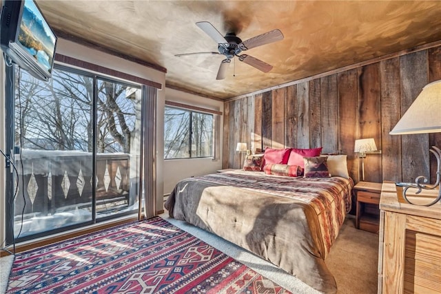 bedroom with carpet flooring, access to exterior, ceiling fan, and wood walls