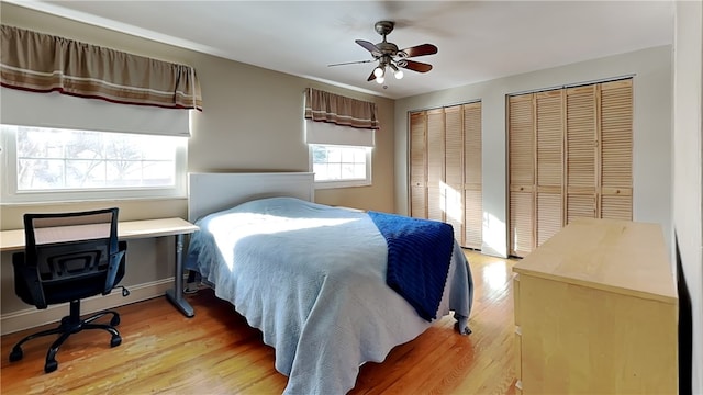 bedroom with ceiling fan, light wood-type flooring, and two closets