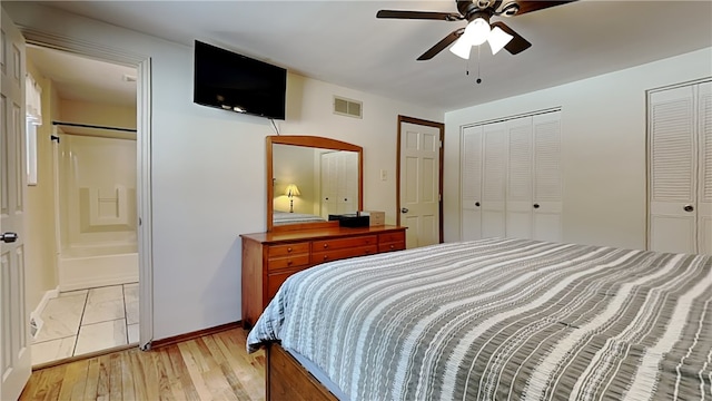 bedroom featuring ensuite bathroom, two closets, ceiling fan, and light hardwood / wood-style flooring