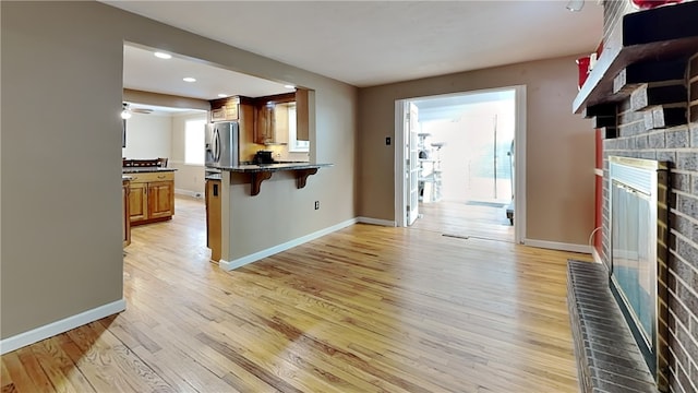 kitchen featuring stainless steel refrigerator with ice dispenser, a kitchen bar, stone countertops, a brick fireplace, and light wood-type flooring