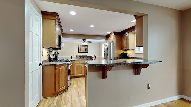 kitchen with light wood-type flooring, a breakfast bar area, kitchen peninsula, and appliances with stainless steel finishes