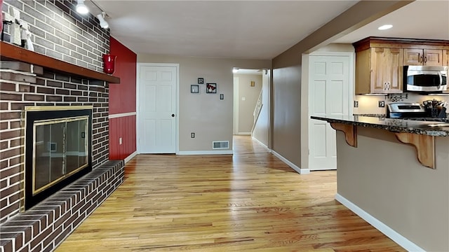 living room with track lighting, a brick fireplace, and light wood-type flooring