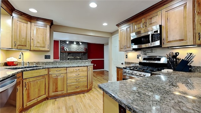 kitchen with appliances with stainless steel finishes, light hardwood / wood-style floors, sink, and dark stone counters