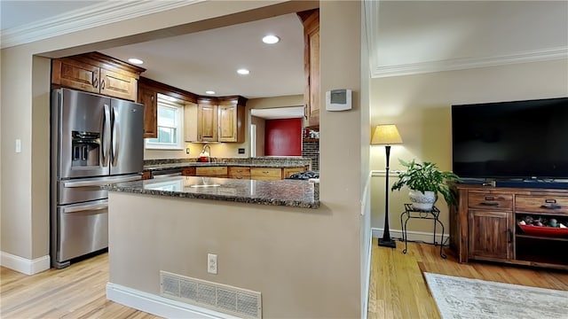 kitchen with stainless steel fridge, light hardwood / wood-style floors, ornamental molding, kitchen peninsula, and dark stone counters