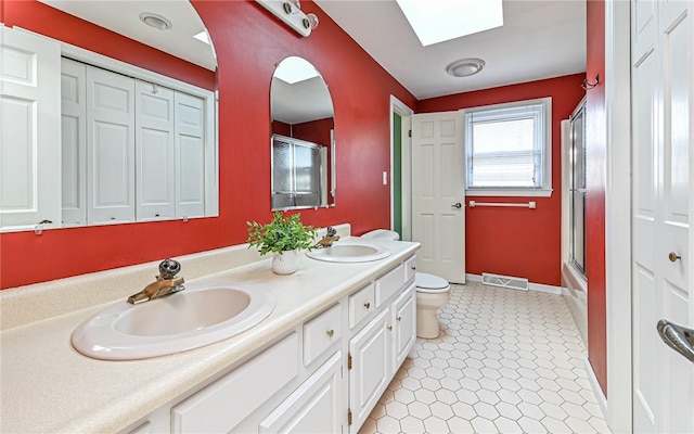 full bathroom with combined bath / shower with glass door, a skylight, vanity, tile patterned floors, and toilet