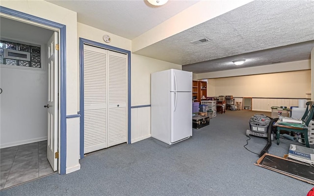 interior space featuring dark colored carpet, white fridge, and a textured ceiling