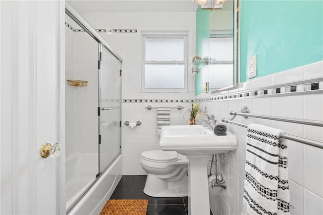 bathroom with tile patterned flooring, toilet, tile walls, and combined bath / shower with glass door