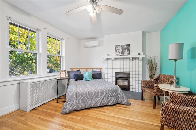 bedroom featuring a wall mounted air conditioner, radiator heating unit, ceiling fan, and light wood-type flooring