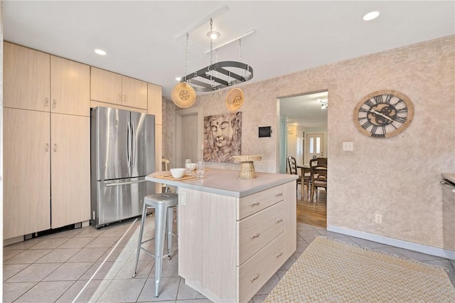 kitchen with a kitchen bar, a center island, light tile patterned floors, stainless steel refrigerator, and light brown cabinets