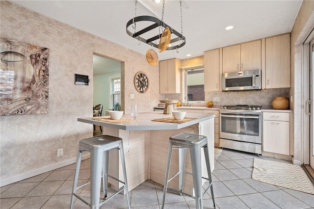 kitchen with light tile patterned floors, a breakfast bar area, appliances with stainless steel finishes, light brown cabinetry, and kitchen peninsula