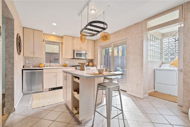 kitchen with light tile patterned flooring, washer / clothes dryer, a center island, stainless steel appliances, and light brown cabinets