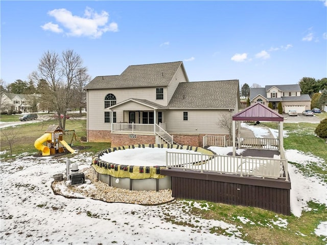 snow covered rear of property featuring a playground, a gazebo, and a wooden deck