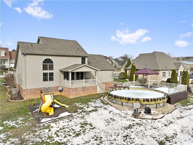 snow covered back of property featuring a playground, a gazebo, and a covered pool