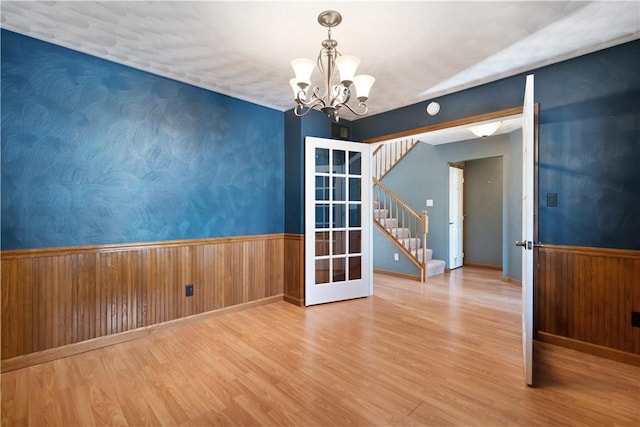 unfurnished room with a notable chandelier, wood-type flooring, french doors, and wood walls