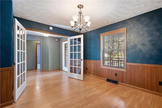 unfurnished dining area featuring hardwood / wood-style floors, an inviting chandelier, and french doors