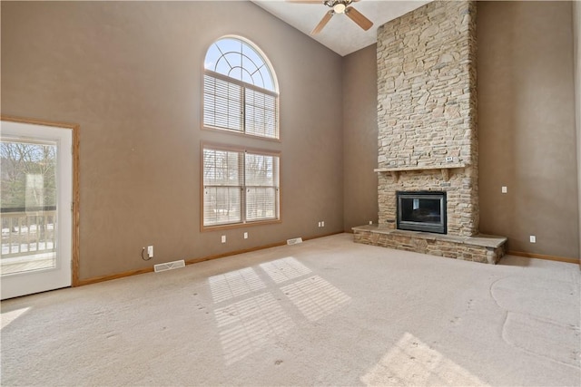 unfurnished living room with light carpet, a stone fireplace, ceiling fan, and a towering ceiling