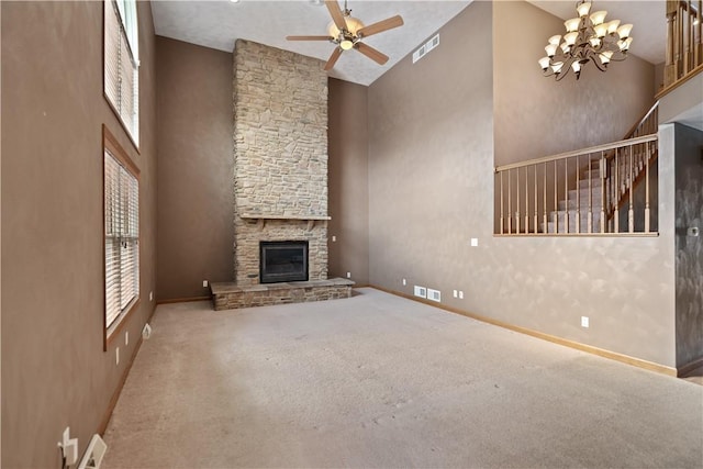 unfurnished living room with a stone fireplace, carpet floors, ceiling fan with notable chandelier, and a towering ceiling