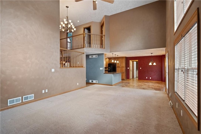 unfurnished living room with a high ceiling, ceiling fan with notable chandelier, and light carpet