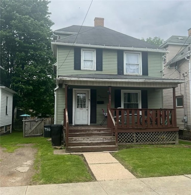 american foursquare style home with a chimney, covered porch, a gate, and a front lawn