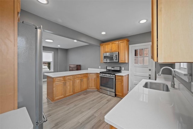 kitchen with appliances with stainless steel finishes, sink, light hardwood / wood-style flooring, and kitchen peninsula