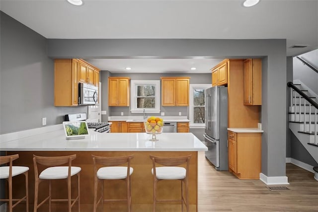 kitchen with light wood finished floors, a peninsula, stainless steel appliances, light countertops, and recessed lighting