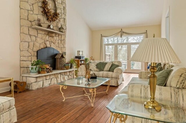 living room with hardwood / wood-style flooring, a stone fireplace, and high vaulted ceiling