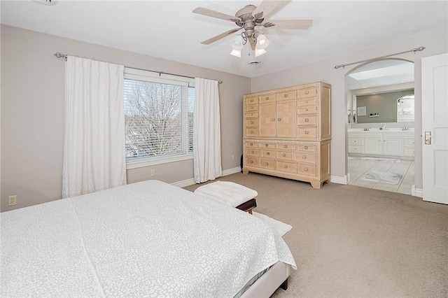 bedroom with ceiling fan, light colored carpet, and ensuite bath