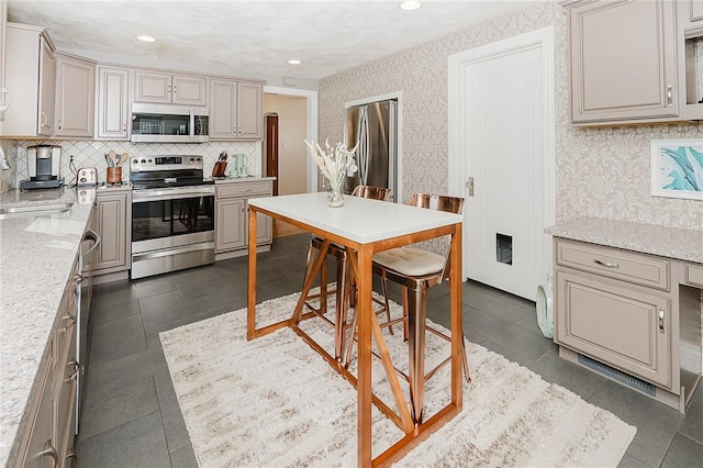 kitchen with sink, dark tile patterned floors, stainless steel appliances, light stone counters, and tasteful backsplash