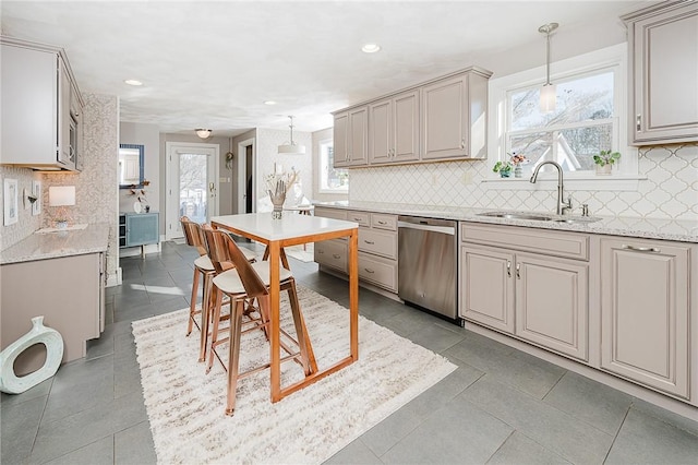 kitchen featuring sink, stainless steel dishwasher, light stone counters, and decorative light fixtures