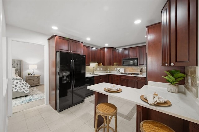 kitchen with sink, a breakfast bar, backsplash, black appliances, and kitchen peninsula