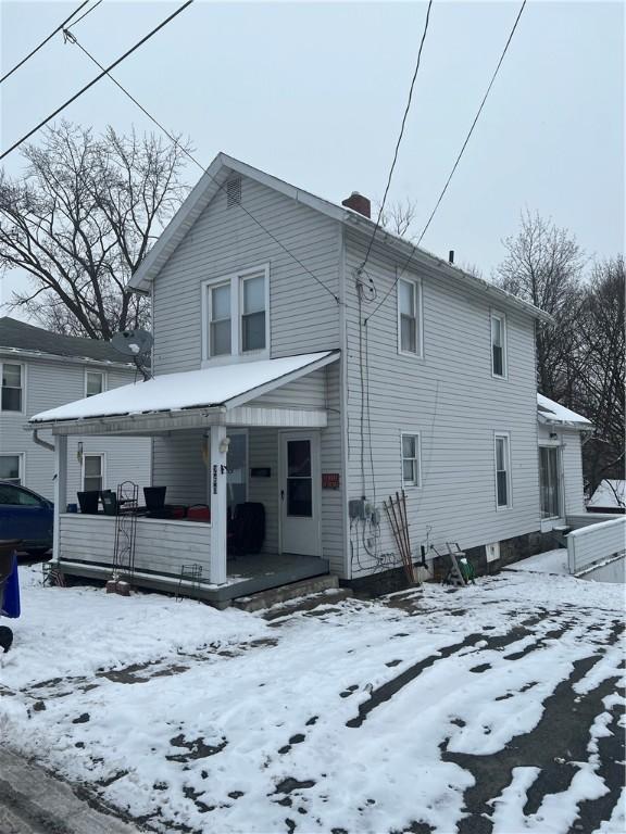 snow covered back of property featuring a porch and a chimney