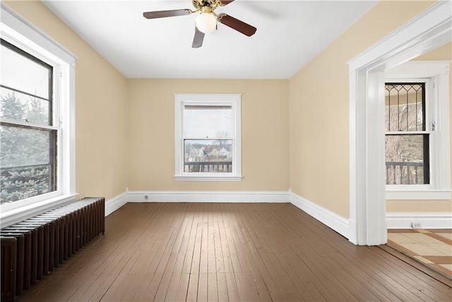 spare room featuring hardwood / wood-style floors, radiator heating unit, a healthy amount of sunlight, and ceiling fan