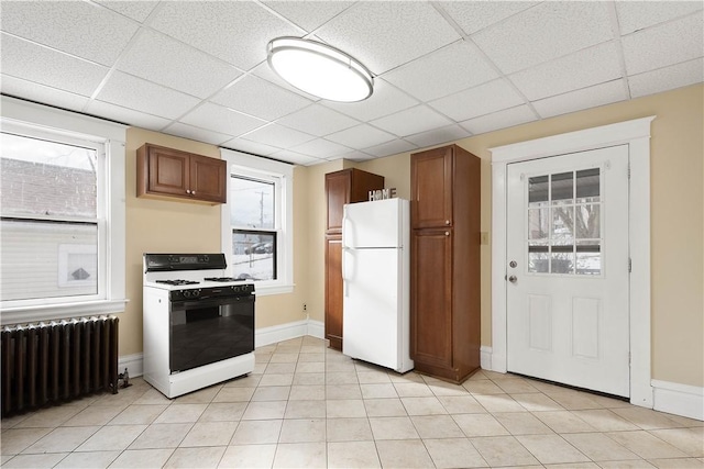 kitchen featuring white refrigerator, radiator heating unit, gas range, and a drop ceiling