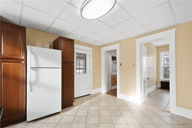 kitchen featuring white refrigerator, radiator, light tile patterned floors, and a drop ceiling