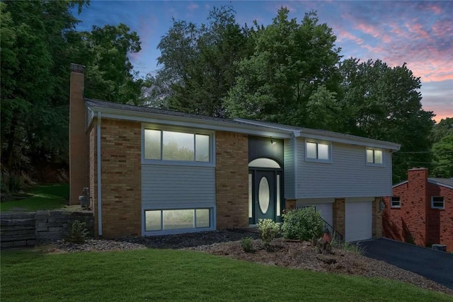 raised ranch featuring a garage and a lawn