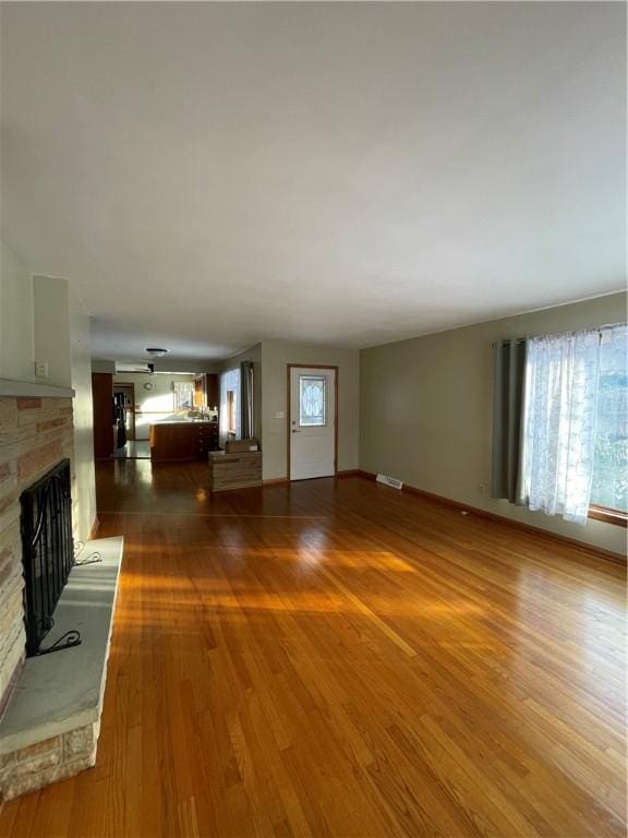 unfurnished living room featuring a stone fireplace and dark hardwood / wood-style flooring