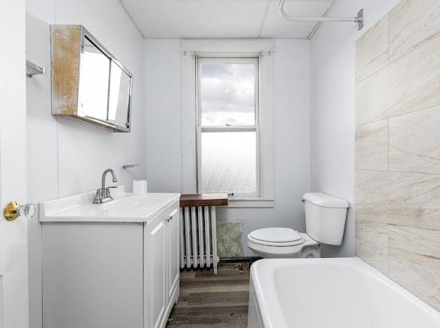 bathroom featuring toilet, vanity, radiator, a bathtub, and hardwood / wood-style flooring