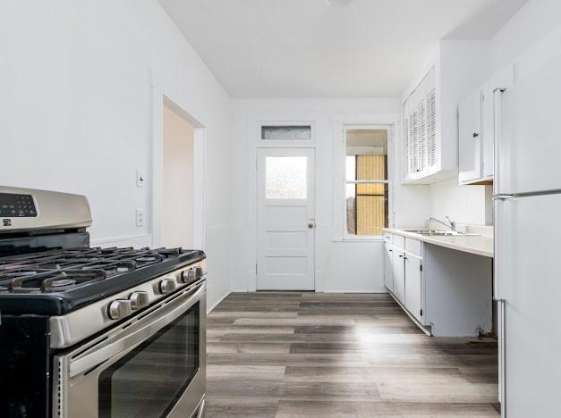 kitchen featuring stainless steel gas range, sink, white cabinetry, dark hardwood / wood-style flooring, and white fridge