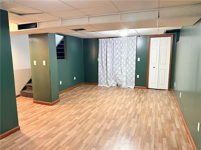 basement featuring a paneled ceiling and light hardwood / wood-style floors