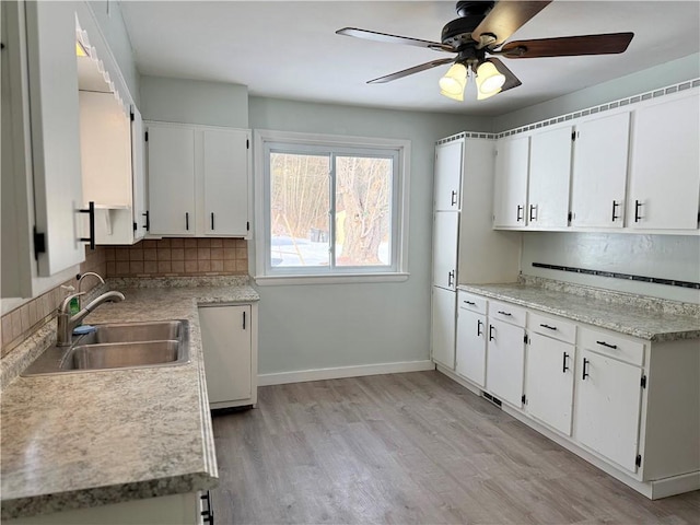 kitchen with sink, light hardwood / wood-style flooring, ceiling fan, backsplash, and white cabinets