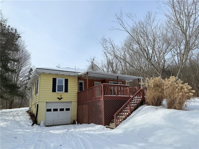 snow covered property with a wooden deck and a garage