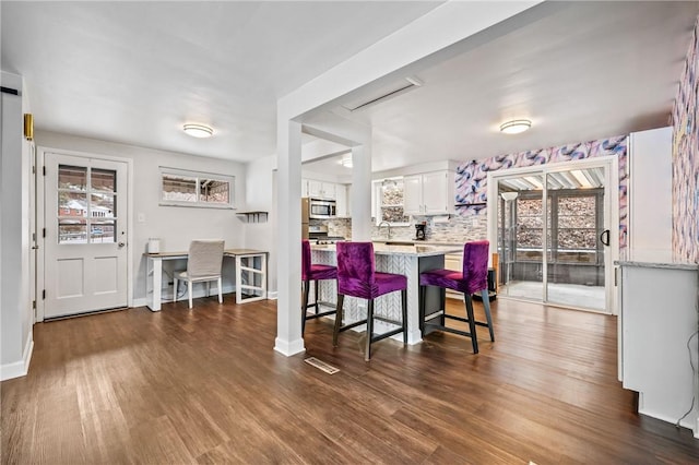 kitchen with backsplash, white cabinets, a kitchen bar, stainless steel appliances, and dark wood-type flooring