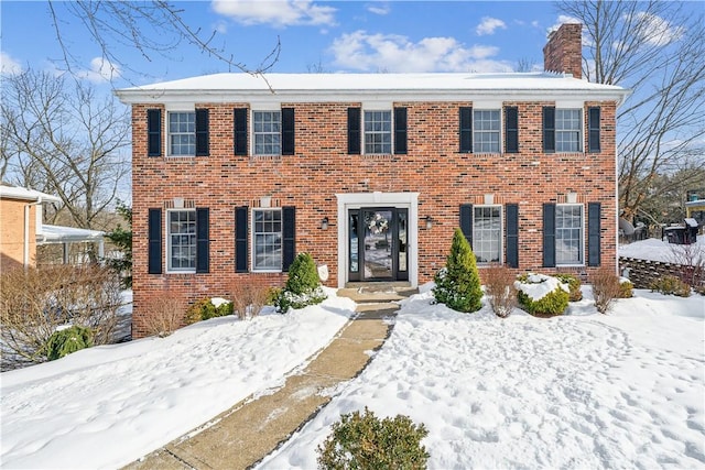 colonial inspired home featuring a chimney and brick siding