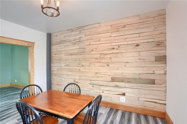 dining room with wood-type flooring, wooden walls, and a chandelier