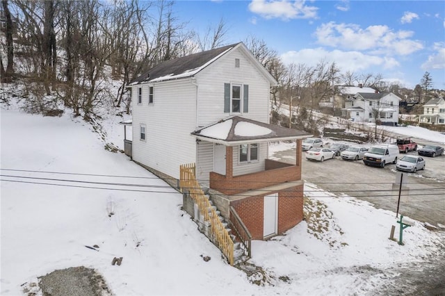 view of snowy exterior with brick siding, a residential view, and stairs