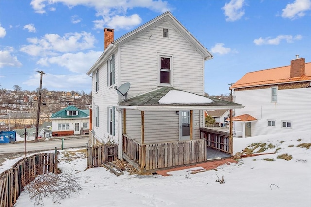 snow covered rear of property with fence and a chimney