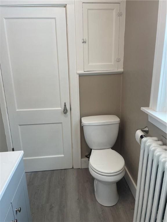 bathroom with baseboards, radiator, wood finished floors, and toilet