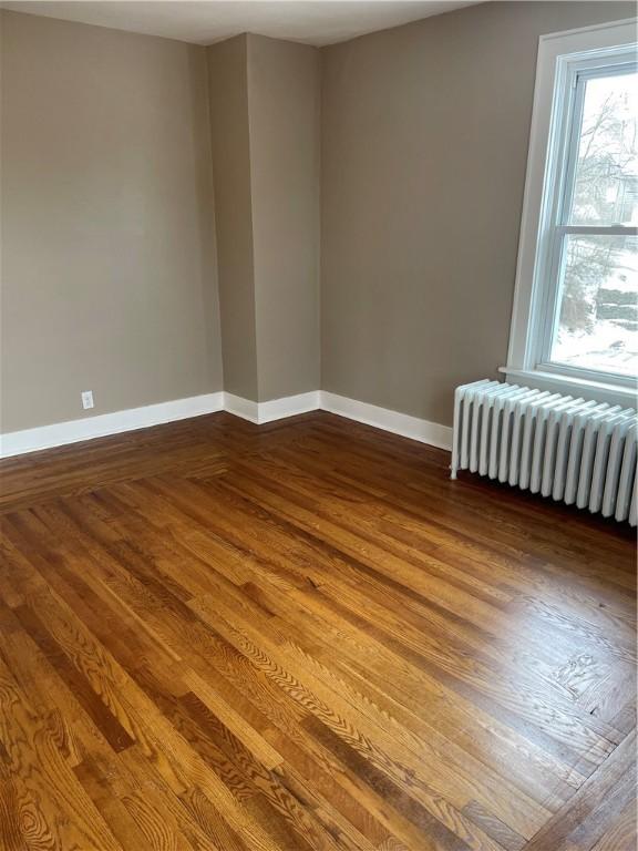 spare room with radiator, baseboards, and dark wood-style flooring